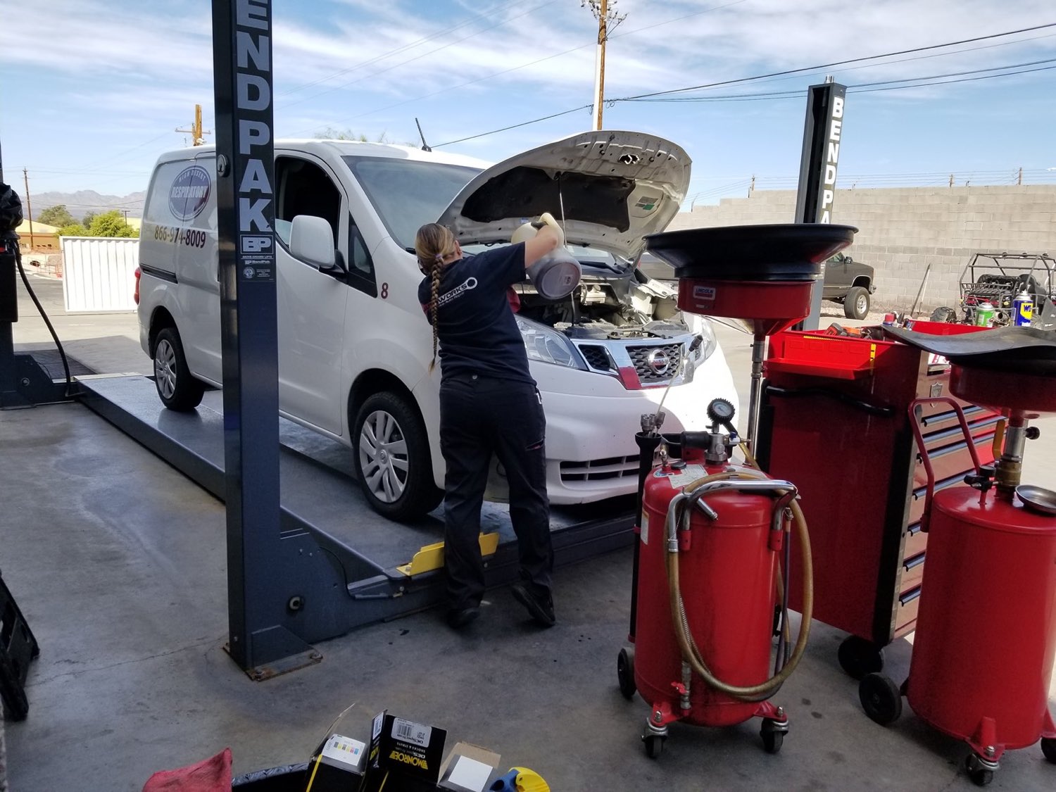 Autoworks tech pouring fresh oil on a work van up on the lift