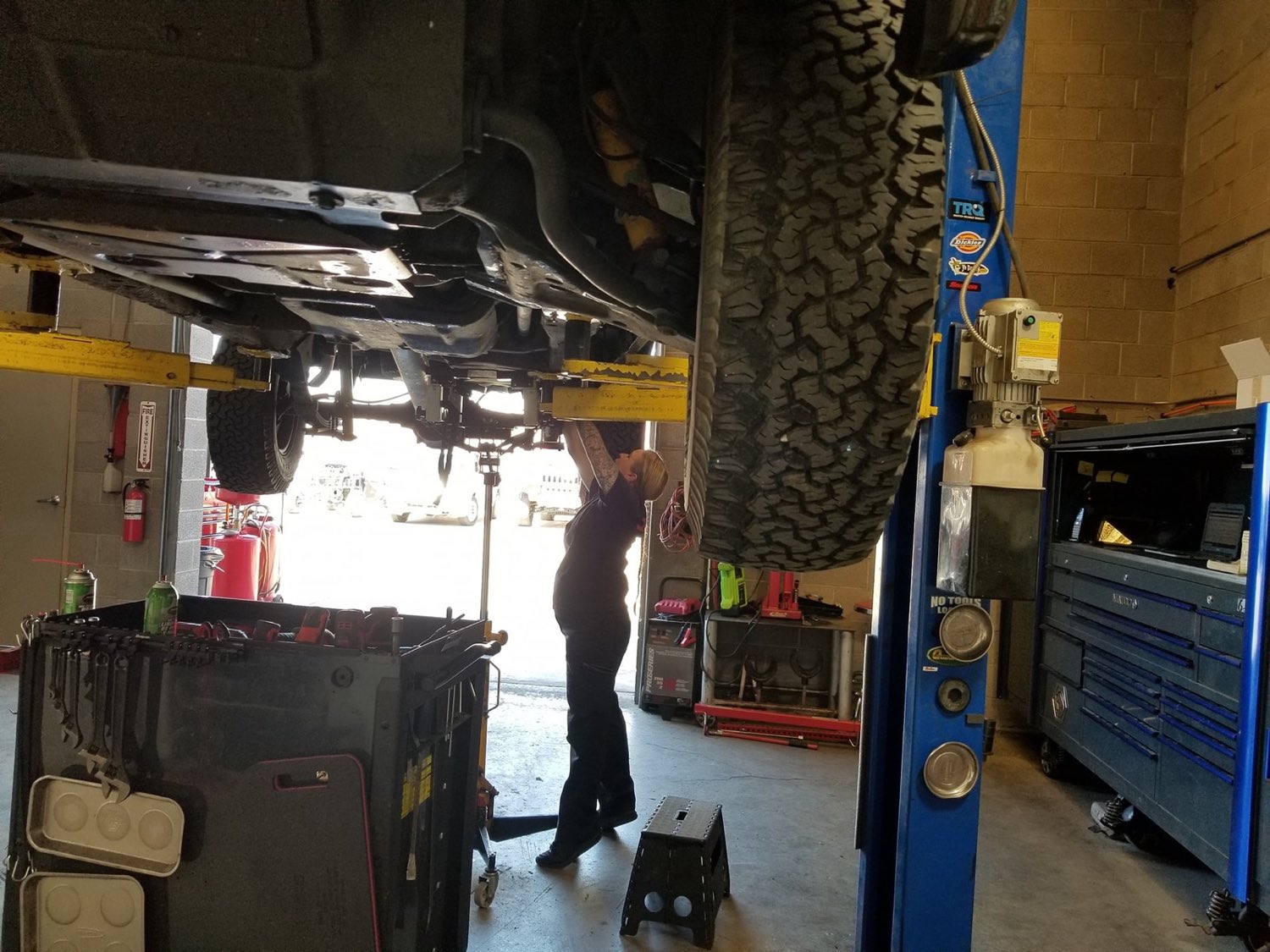 Autoworks technician working under a lifted 4x4 inside the shop